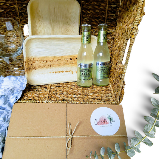 Picnic for two charcuterie set with bamboo plates, ginger beer bottles, and a boxed grazing package.